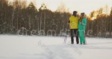 在日落时分的冬季森林里，一男一女一滑雪，看着大自然的美景和慢镜头